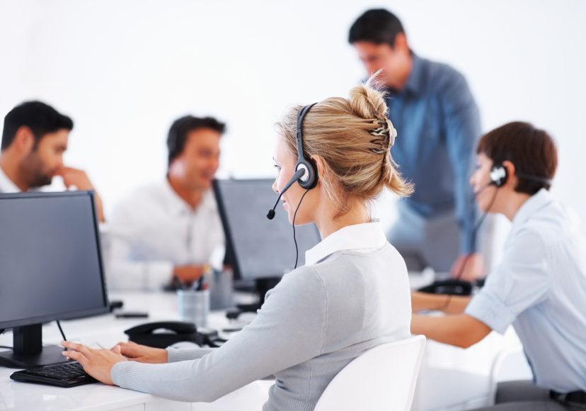 Business woman wearing headset working on computer with colleagues in background